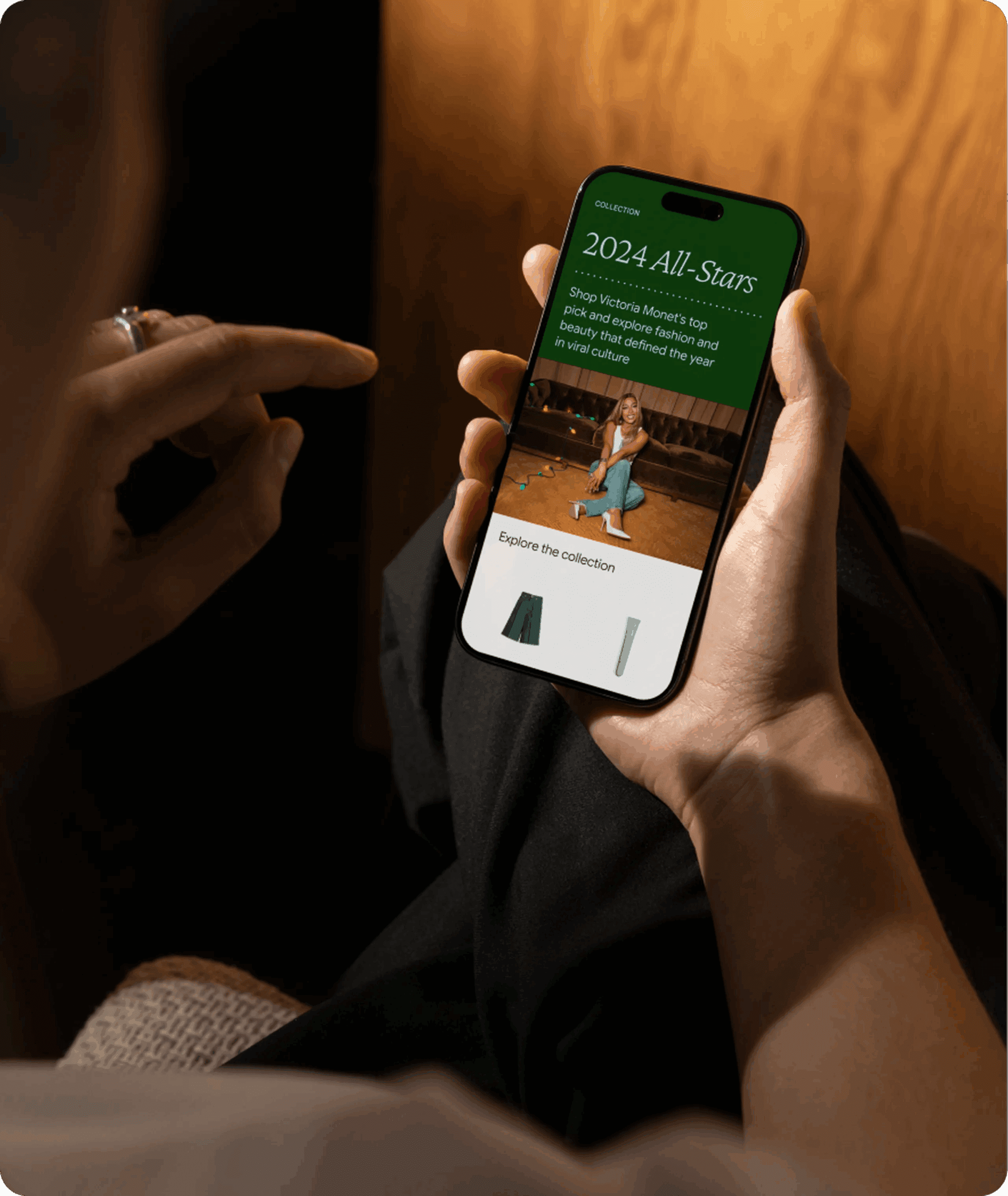 Person holding a smartphone displaying a webpage titled "2024 All-Stars," featuring a photo of a woman sitting on the floor and text promoting a fashion collection, with options to explore items below.