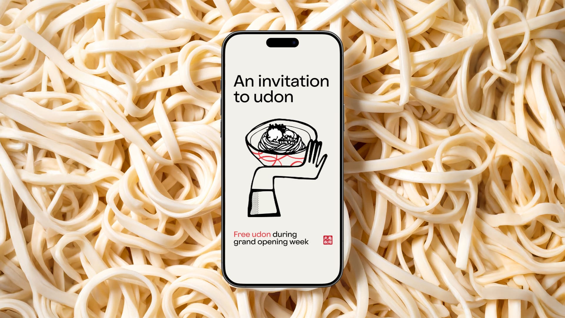 A smartphone displays an udon restaurant invitation, featuring a bowl of noodles graphic and text offering free udon during grand opening week. The phone lies on a background of uncooked udon noodles.