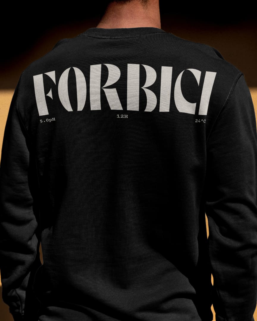 A person wearing a black sweatshirt seen from behind. The back of the sweatshirt features bold white text reading "FORBICI" along with smaller text displaying numbers and symbols underneath.