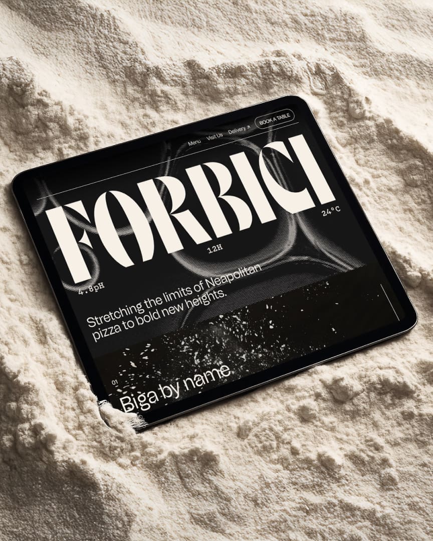 A tablet displaying a website with bold text reading "FORBICI" lies partially buried in a mound of flour, emphasizing a connection to baking or pizza-making.
