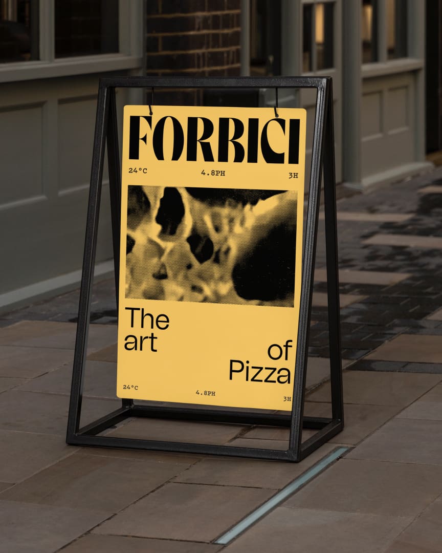 A sandwich board sign with a yellow poster reads "FORBICI" at the top and "The art of Pizza" at the bottom, featuring an abstract, black-and-yellow image of pizza in the center. The sign stands on a stone sidewalk.