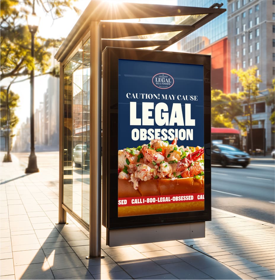 A bus stop advertisement shows a sandwich with the text: "Caution: May Cause Legal Obsession" and "LEGAL OBSESSION." A phone number, 1-800-LEGAL-OBSESSED, is displayed below. City buildings and sunlight are in the background.